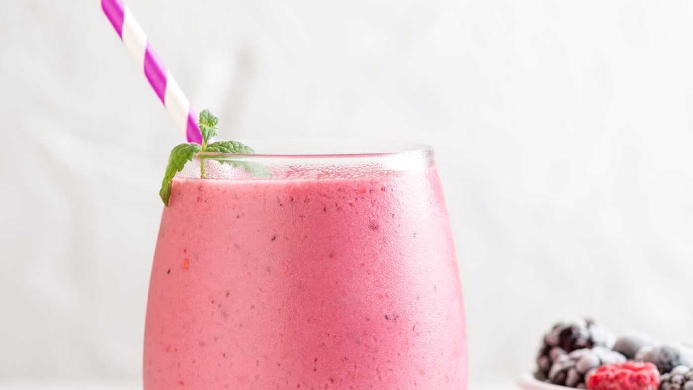 A vertical shot of a delicious mix berry milkshake with different berries in a bowl next to it