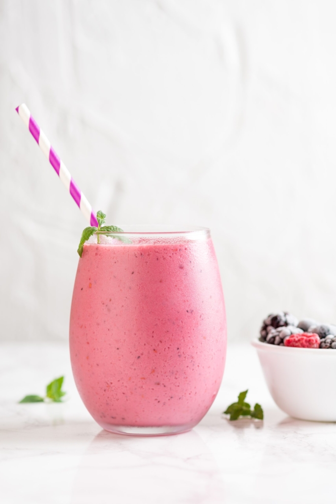 A vertical shot of a delicious mix berry milkshake with different berries in a bowl next to it